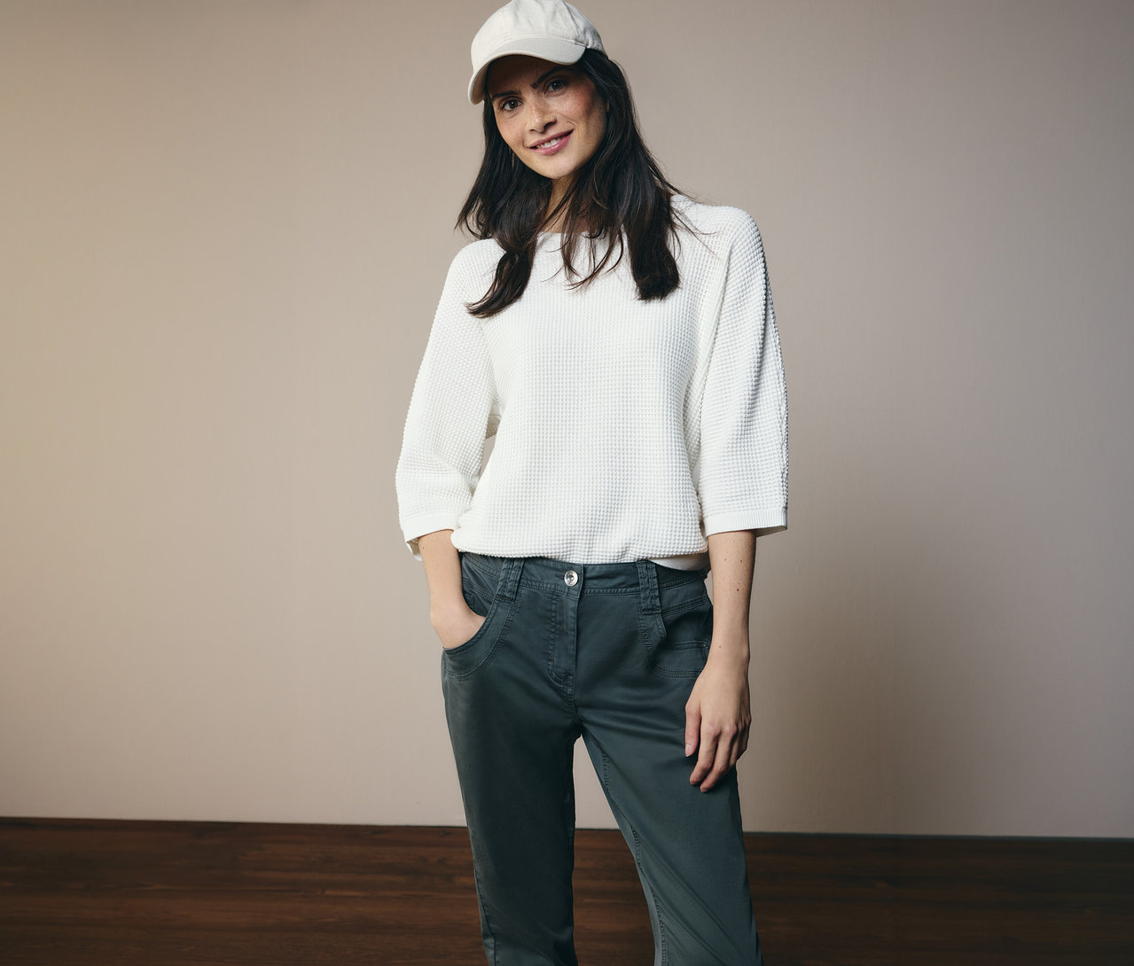 Frau mit weißem Oberteil und Kappe posiert in CECIL Hose »Scarlett« mit Händen in den Taschen.