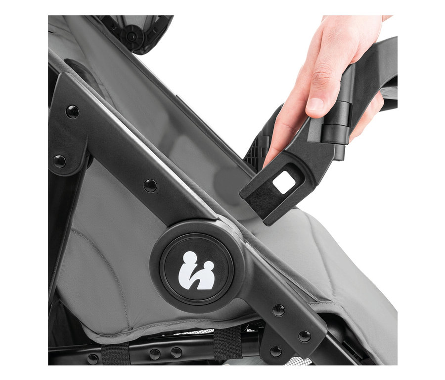 Nahaufnahme eines grauen Kinderwagens, an dem eine Hand ein schwarzes Zubehörteil befestigt.