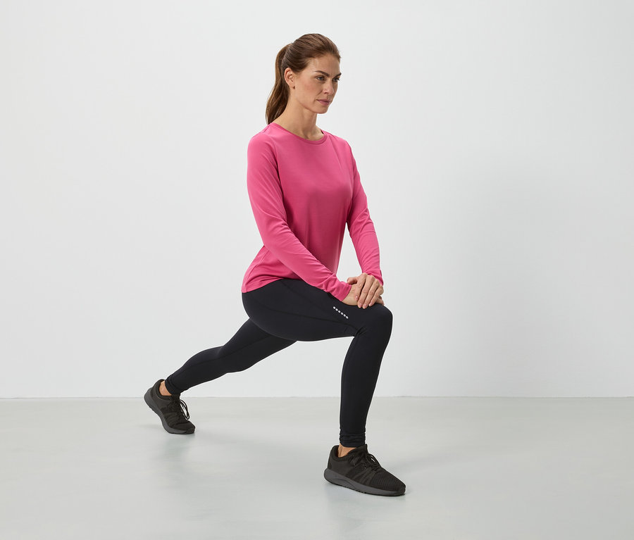 Frau in pinkem Oberteil und schwarzen Leggings dehnt sich.