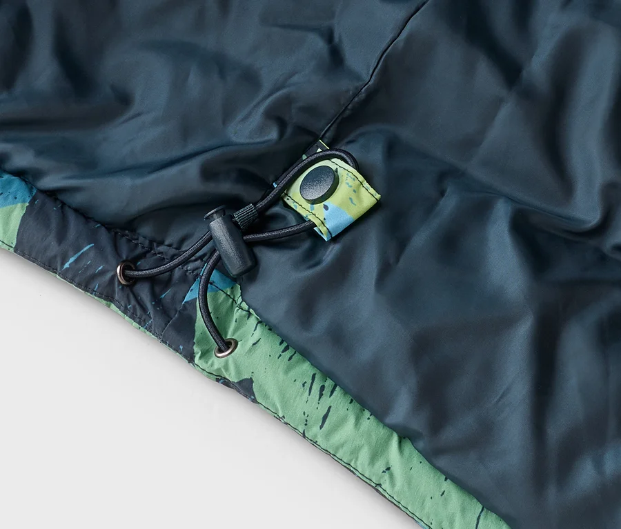Nahaufnahme einer dunkelblau-grünen Jacke mit grün-blau gemustertem Besatz. Ein schwarzer Kordelzug mit Stopper und ein schwarzer Druckknopf sind sichtbar.