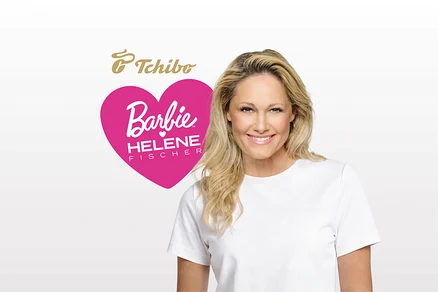 Helene Fischer, eine blonde Frau, lächelt in einem weißen T-Shirt, mit einer pinken Herzgrafik mit der Aufschrift „Barbie HELENE FISCHER“ links von ihr.