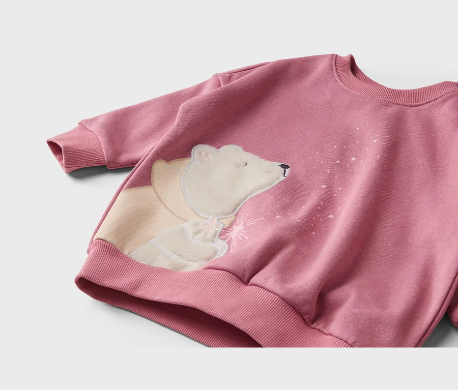 Rosa Sweatshirt mit einem applizierten weißen Eisbären, der einen beigen Umhang trägt und Sterne aus seinem Maul bläst. Rippbündchen an Ärmeln und Saum.