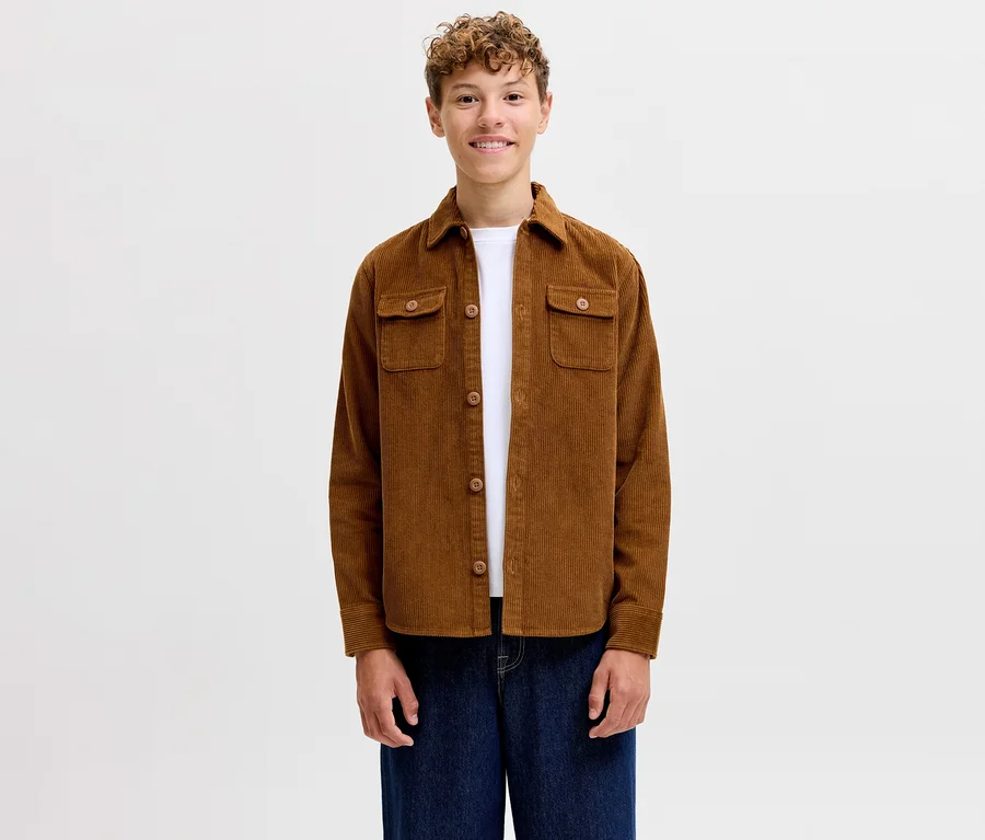 Lächelnder junger Mann trägt ein braunes Jack&Jones Cordhemd Regent über einem weißen T-Shirt und blauen Jeans.
