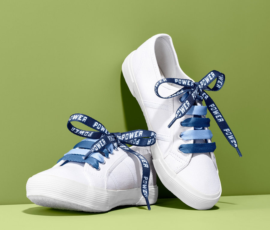 Zwei weiße Schuhe mit blauen Kinder-Schnürsenkel mit Motiv auf grünem Hintergrund.