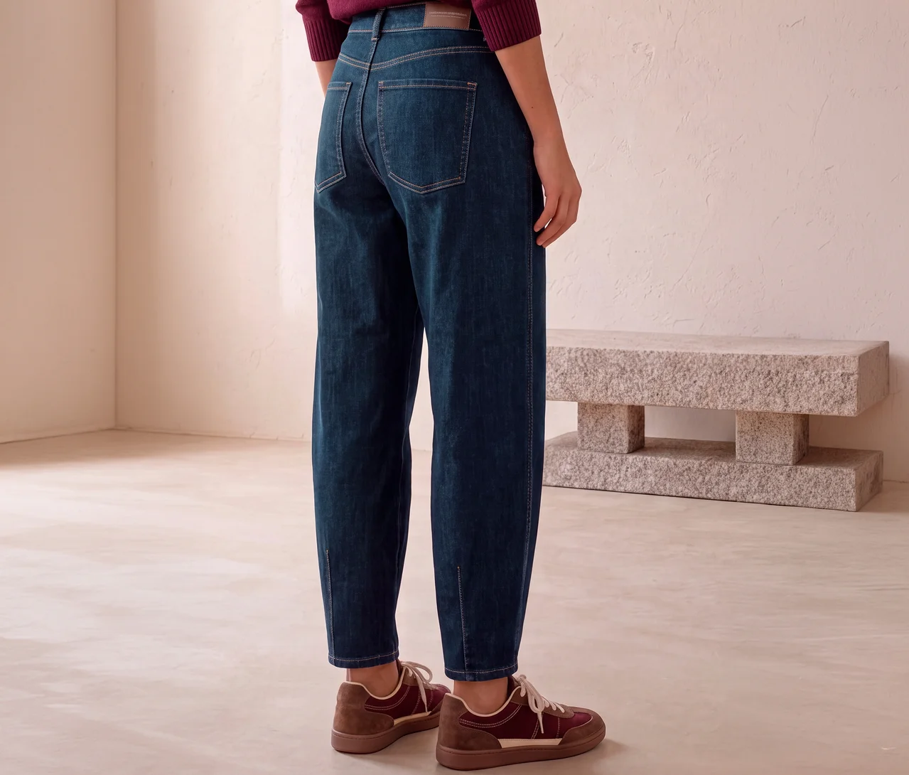 Person trägt dunkelblaue Street One Jeans mit sichtbaren Nähten und braune Sneaker, steht mit dem Rücken zum Betrachter.