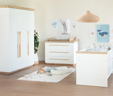 Ein Kinderzimmer mit einem weissen Roba 3-teiligen Kinderzimmer-Set "Lumo", bestehend aus einem Kleiderschrank, einer Wickelkommode und einem Babybett mit Holzdetails. An der Wand hängen Bilder, auf dem Boden liegt ein Teppich mit Spielzeug.