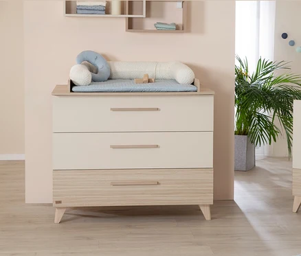 Beige Kommode mit drei Schubladen und einem Wickelaufsatz darauf.