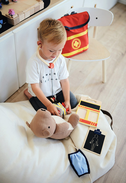 Ein Junge spielt mit einem Teddybär und einem Arztkoffer, trägt ein Stethoskop und daneben liegt ein small foot Notarzt-Rucksack.