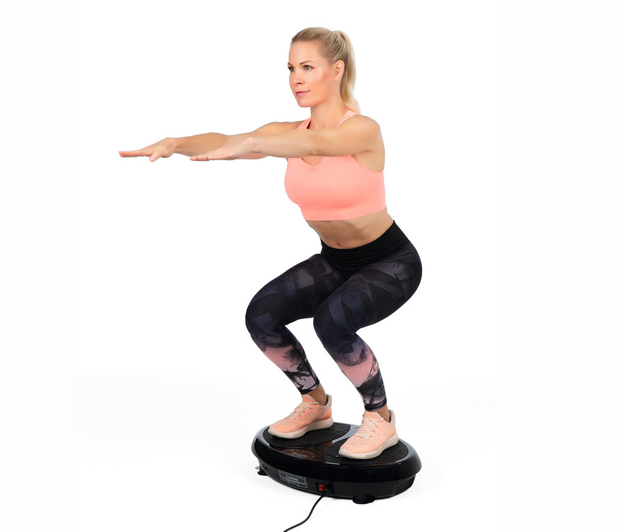 Blonde Frau in rosa Sport-BH und Leggings macht Kniebeugen auf einem VITALmaxx Vibrationstrainer.