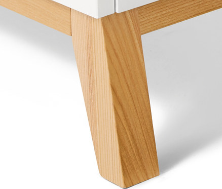 Detail einer weißen Kommode mit hellen Holzbeinen.