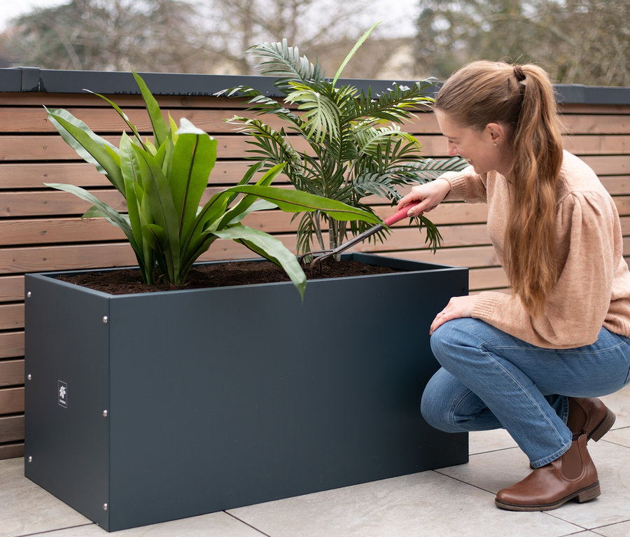 Frau harkt Pflanzen in einem anthrazitfarbenen Herstera Garden Pflanzkasten.