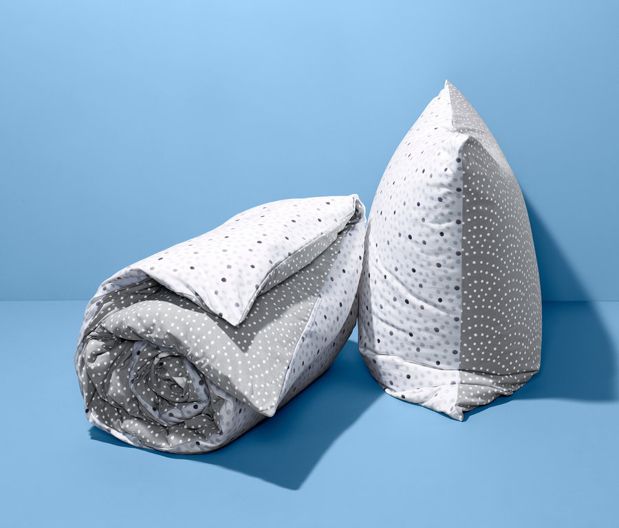 Eine zusammengerollte und gefaltete Jersey-Wendebettwäsche Normalgröße mit Tupfen auf blauem Hintergrund.