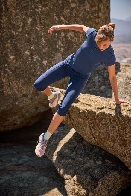 Frau klettert in 3/4-Trekking-Tight und Half-Zip-Sportshirt auf Felsen.
