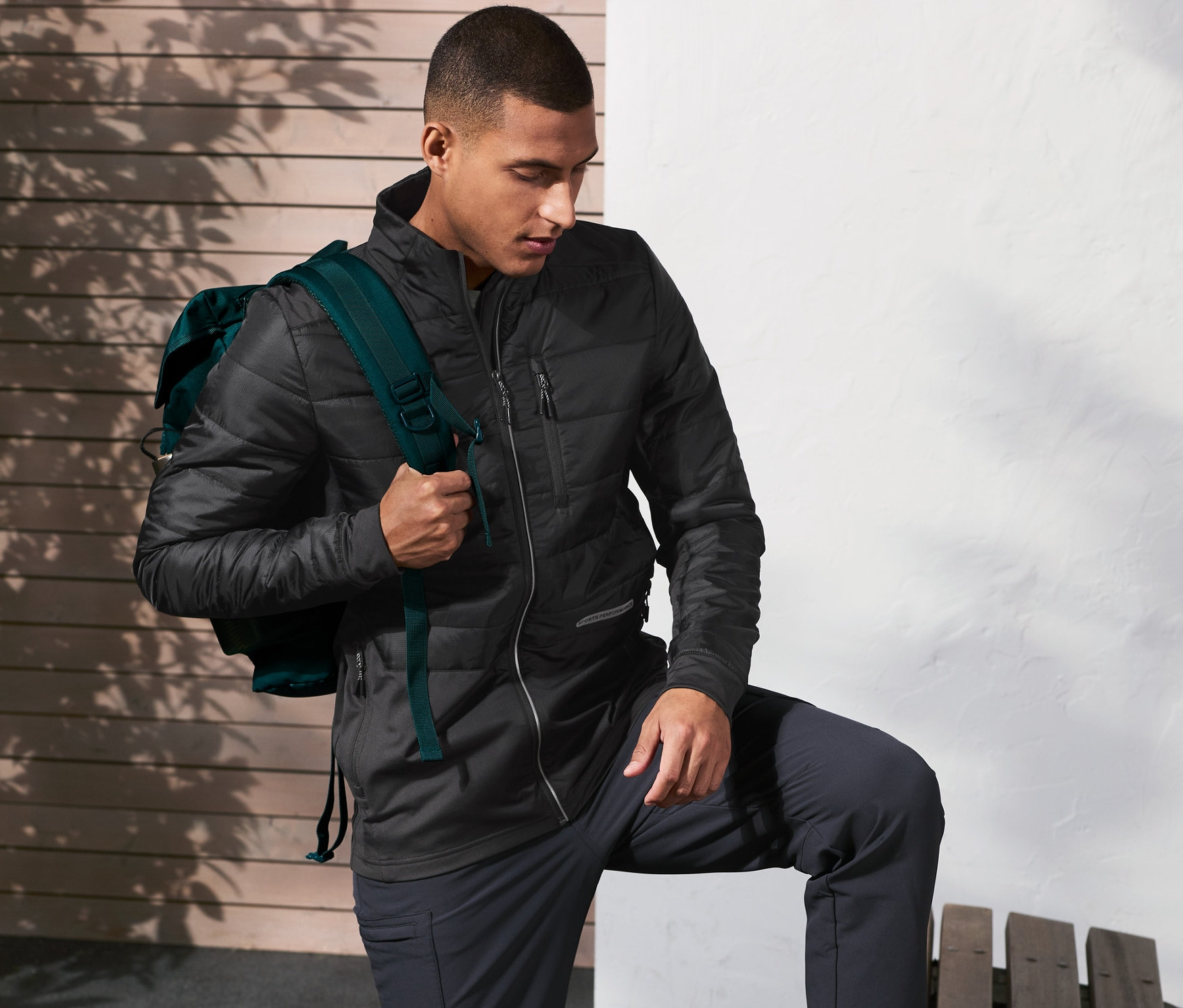 Mann mit Rucksack, der einen Fuß auf eine Bank stellt und eine Thermojacke trägt.