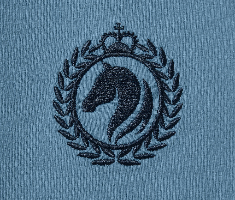 Detail eines blauen Jerseykleids mit einer Stickerei eines Pferdes in einem Kreis mit einer Krone.
