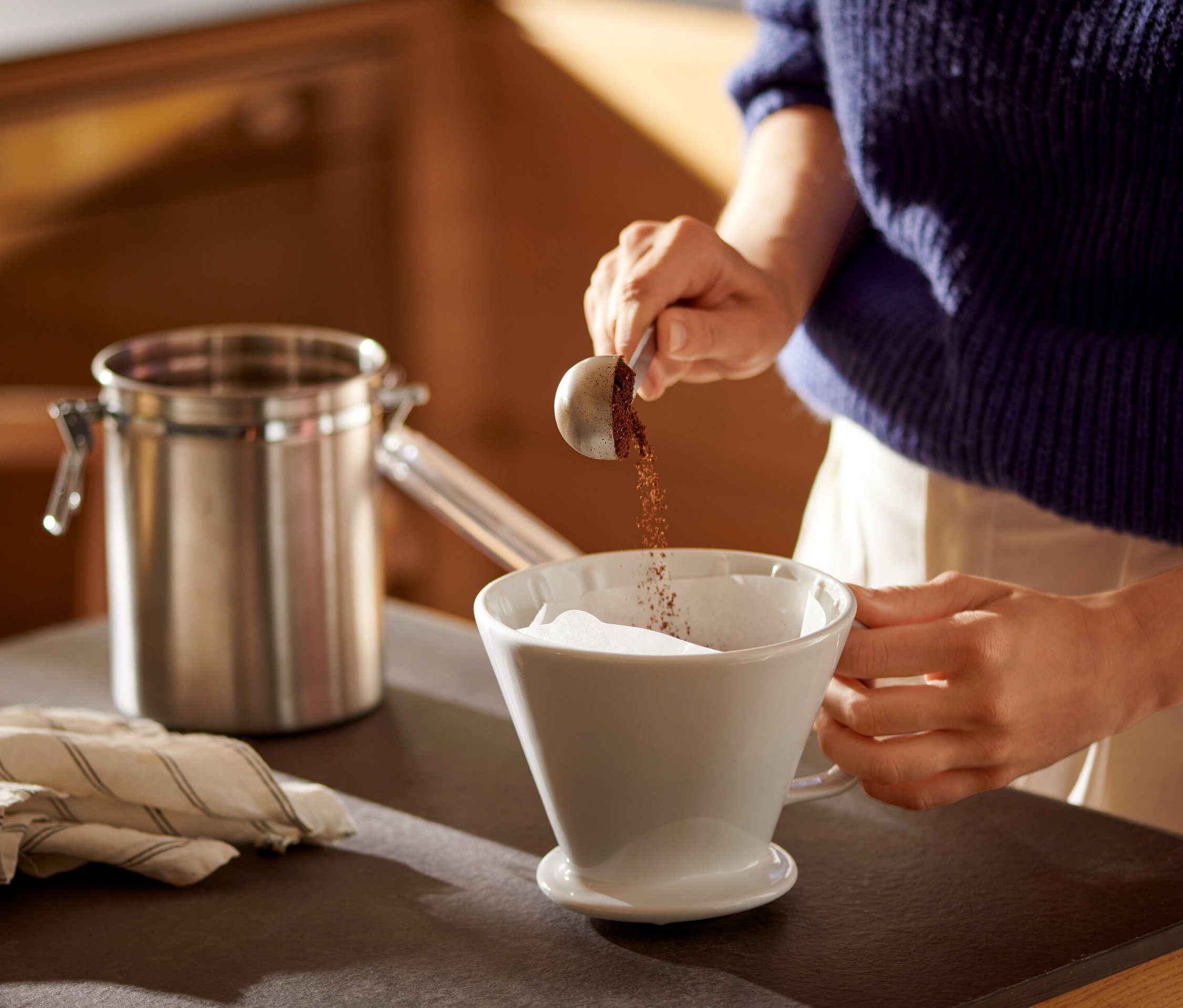 Frau schüttet Kaffee in einen weißen Kaffee Handfilter Gr. 4 mit Kaffeefilterpapier Gr. 4.