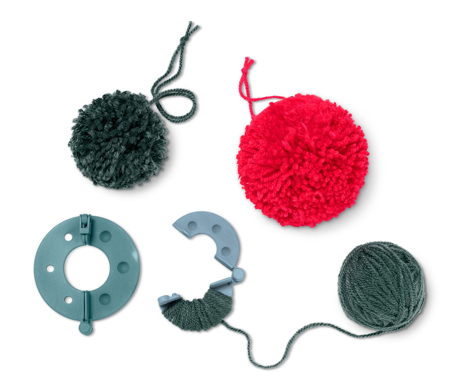 Ansicht eines Bastel-Sets »Bommel-Girlande«, das einen grünen und einen roten Bommel, ein Werkzeug zur Herstellung von Bommeln und ein Knäuel grünes Garn enthält.