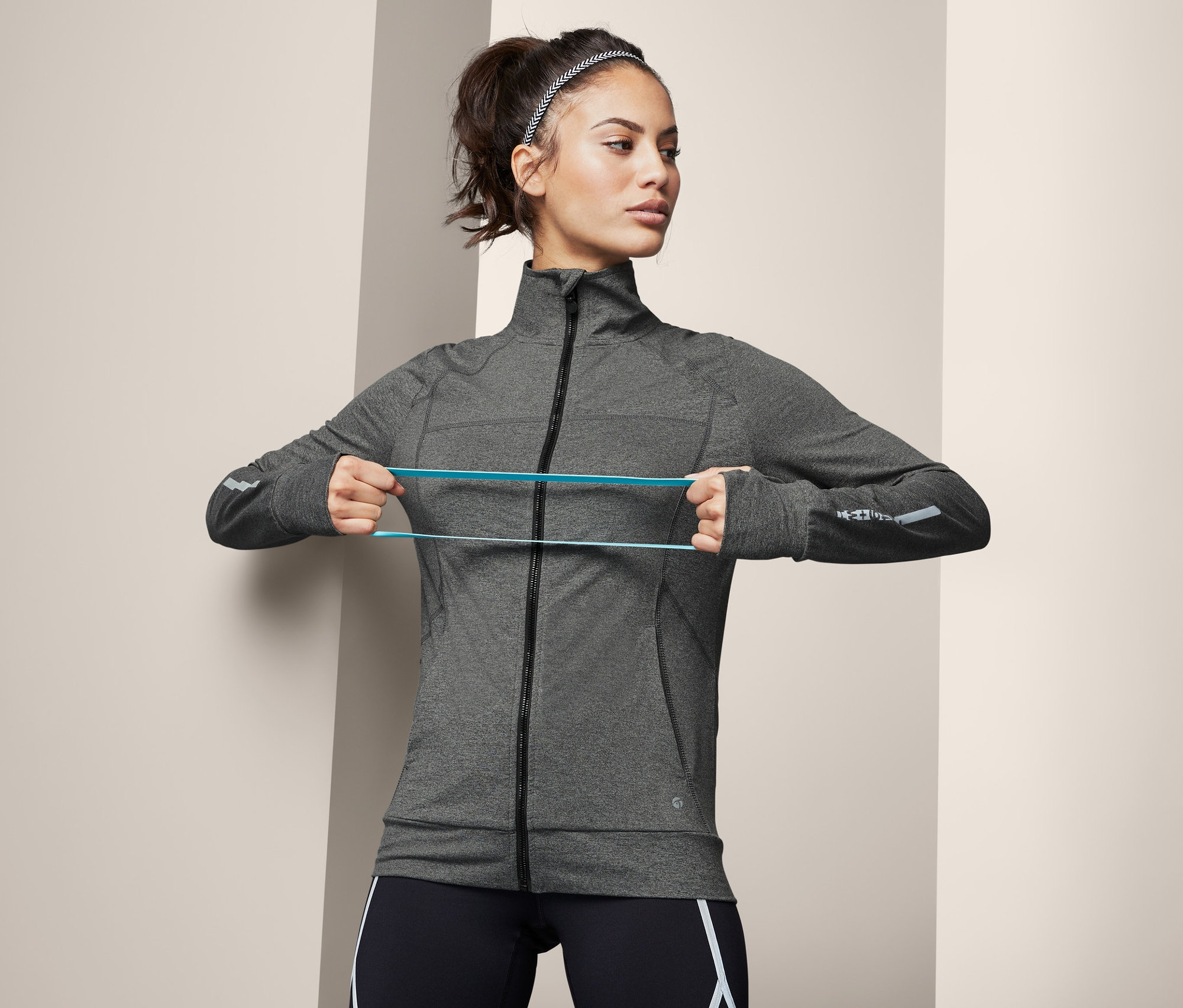 Frau dehnt ein blaues Gummiband, sie trägt eine Funktionsjacke.