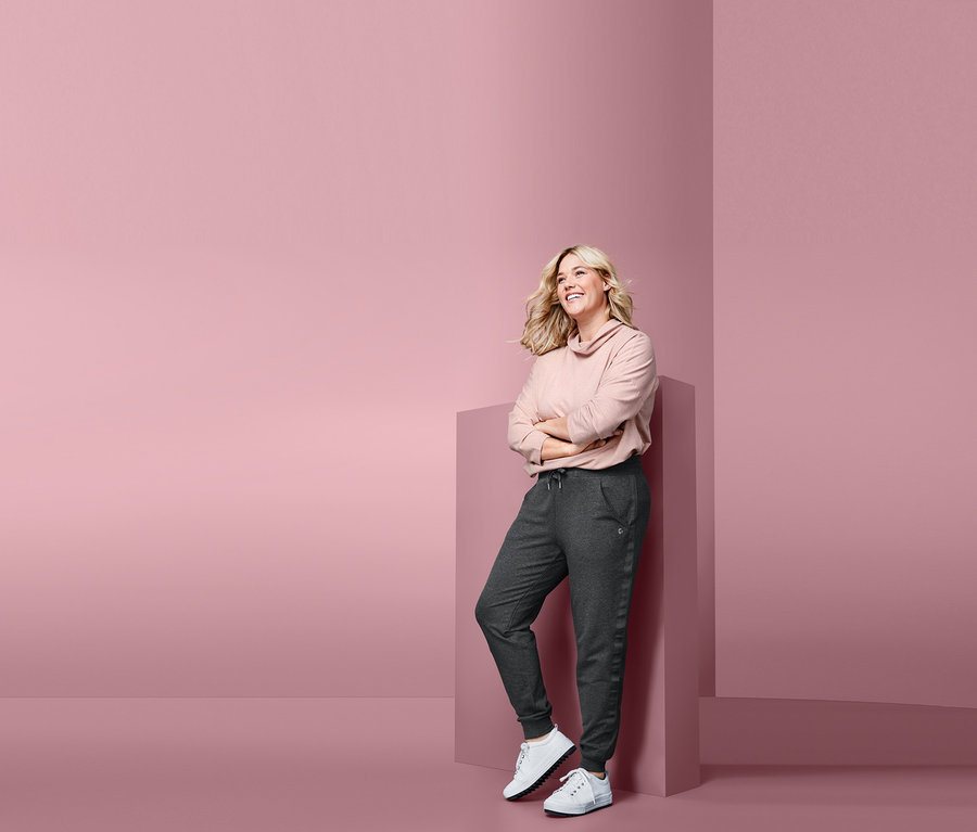 Frau lehnt an einem rosa Quader und trägt eine Sweathose.