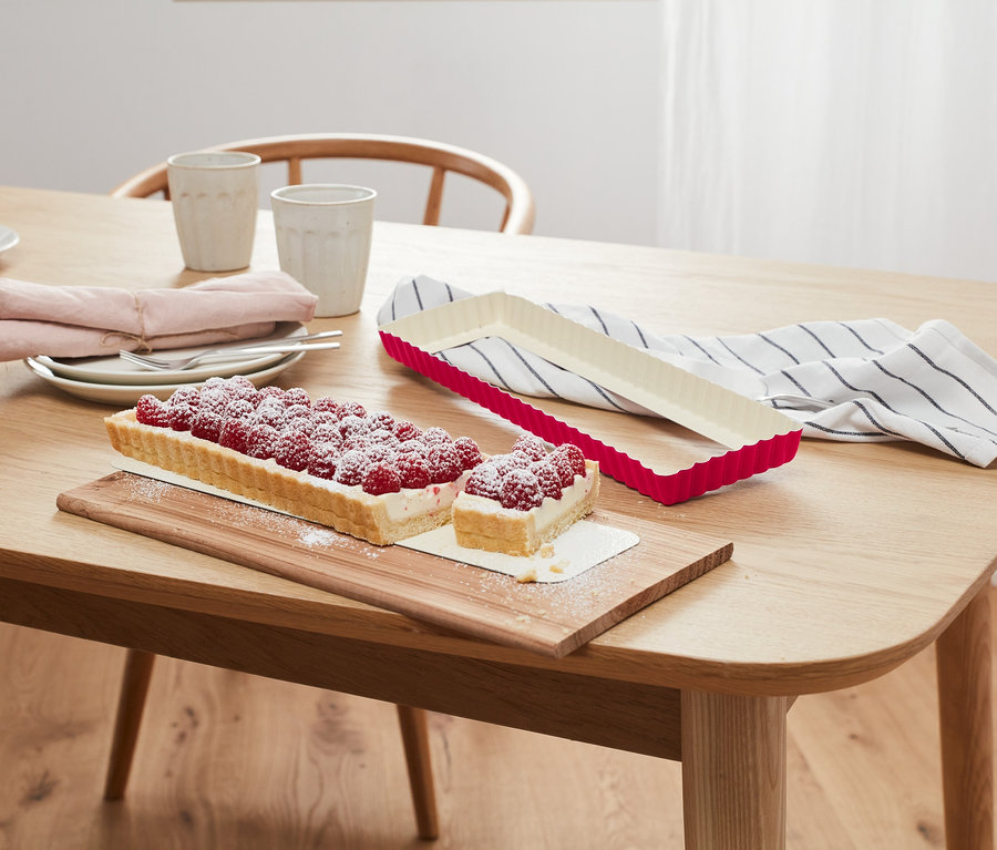 Rechteckige Himbeertarte auf Holzbrett neben Tarteform.