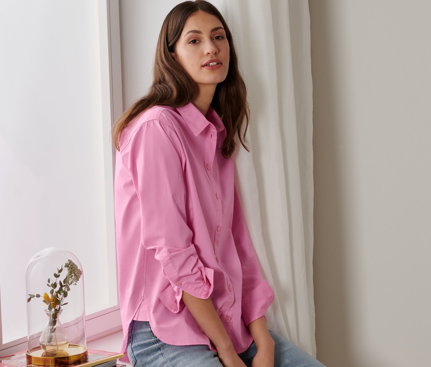 Frau sitzt im Fenster mit einer rosa Hemdbluse.