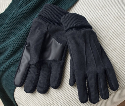 Auf einem beigen Hocker liegen ein Paar schwarze Handschuhe und ein grüner Pullover.