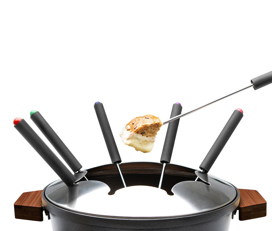 Ein Stück Brot, das in Fondue getunkt ist, wird über einem schwarzen Topf mit farblich gekennzeichneten Gabeln gehalten.