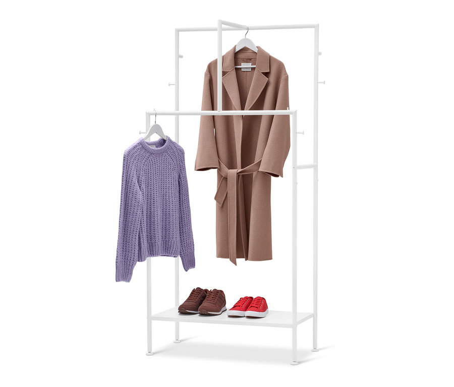 Auf einem weißen Garderobenständer hängen ein lila Pullover und ein brauner Mantel. Auf dem unteren Regal stehen braune und rote Schuhe.