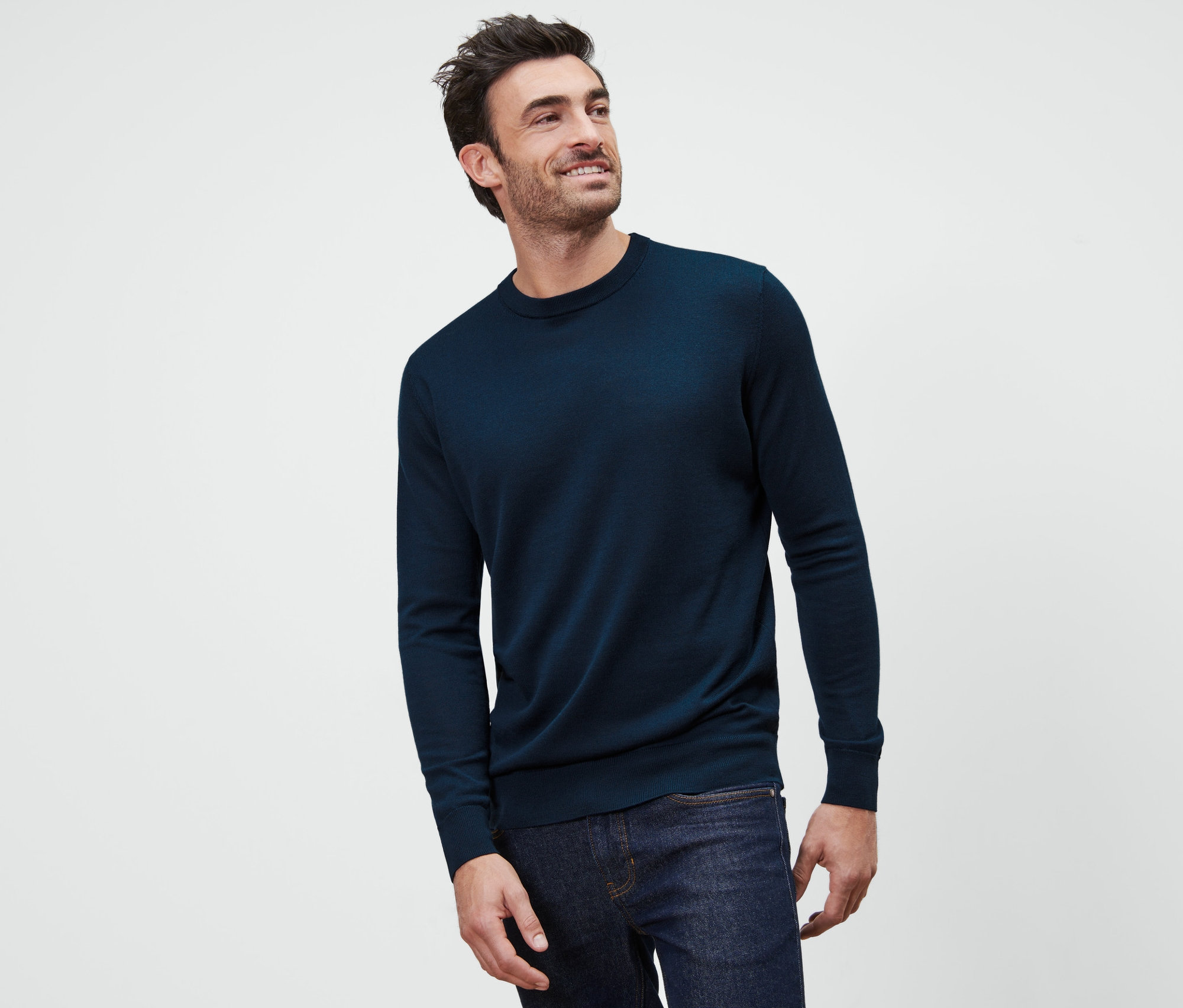 Ein Mann mit braunen Haaren lächelt und trägt einen marineblauen Merino-Pullover.