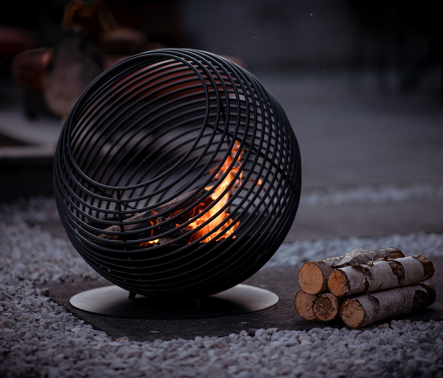 Design-Feuerkorb »Atlas« mit brennendem Holz und einem Holzstapel am Boden.