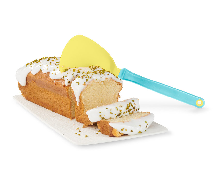 Ein Kuchen mit Guss und Streuseln auf einem Teller, daneben ein gelber Eier-und-Pfannkuchenwender.