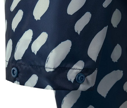 Detailansicht eines blauen Regenponchos mit weißem Muster und Ärmeln, der mit Druckknöpfen geschlossen wird.