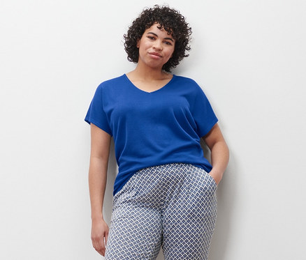 Frau steht mit der Hand in der Tasche einer bedruckten Hose, trägt ein kobaltblaues Shirt und Canvas-Sneaker.