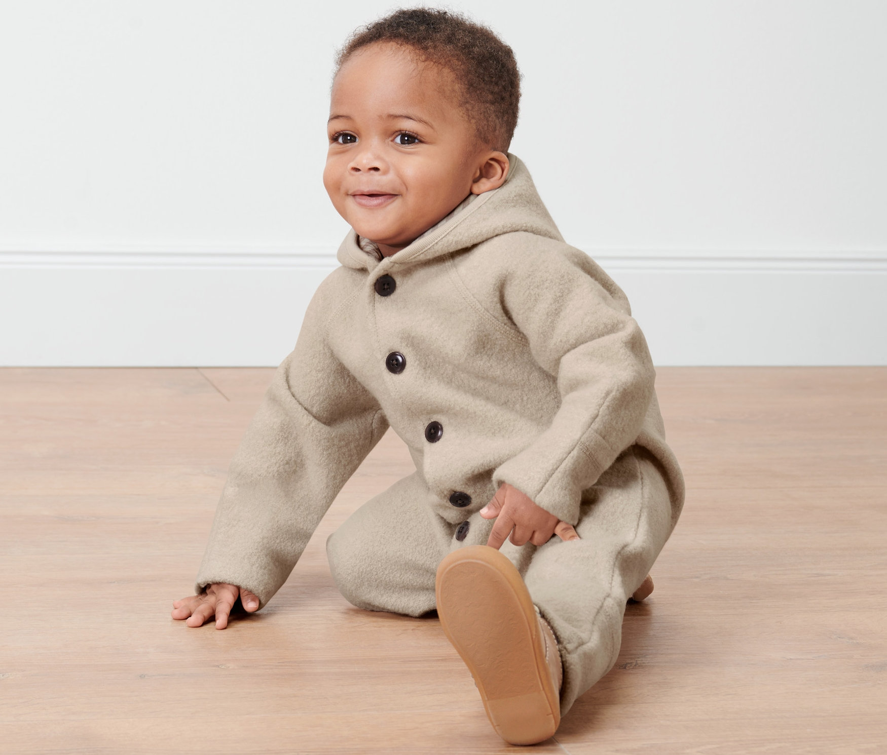 Kleinkind im Baby-Merino-Walkoverall sitzt auf dem Boden.