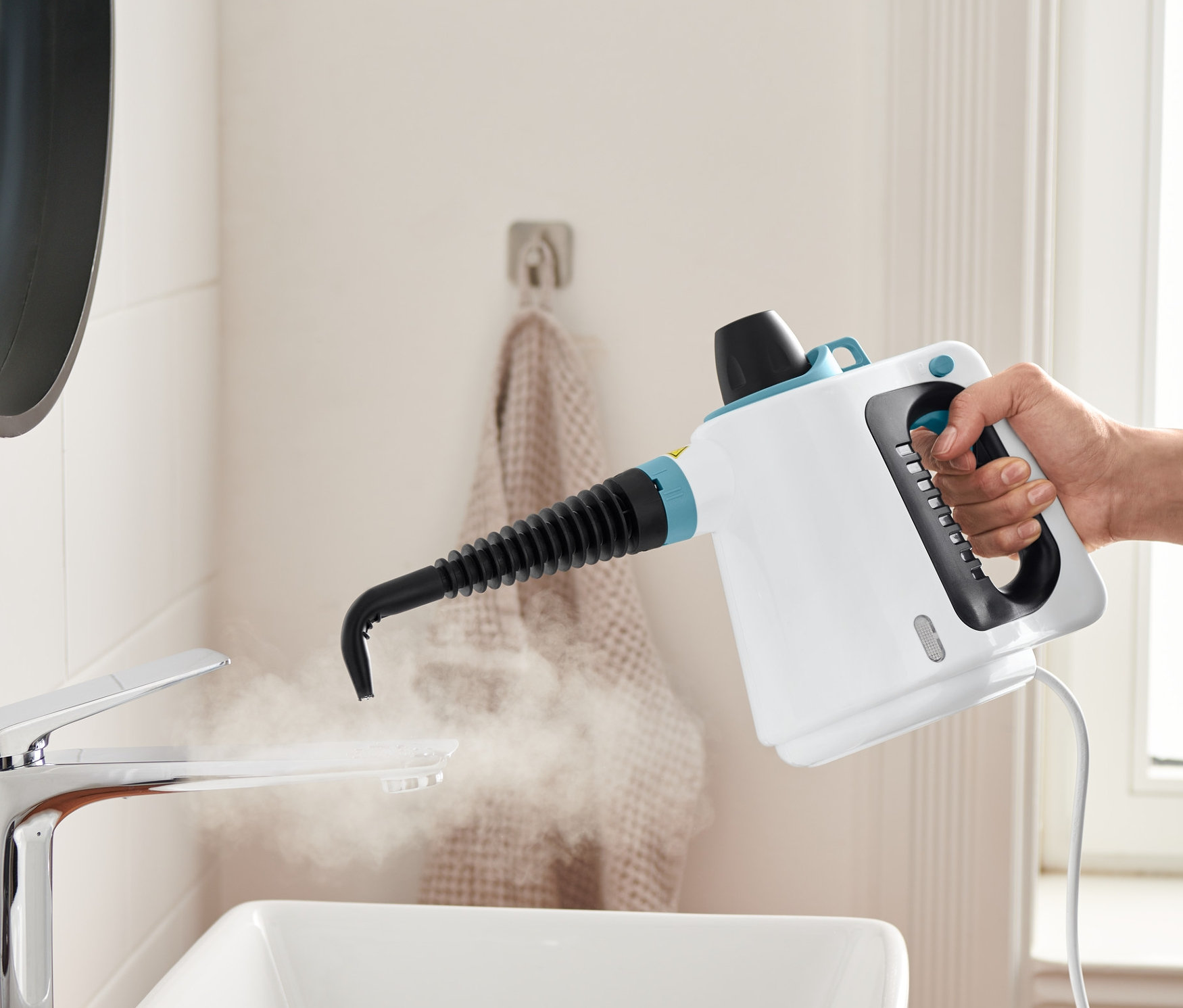 Eine Hand hält einen Dampfreiniger und reinigt damit ein Waschbecken.