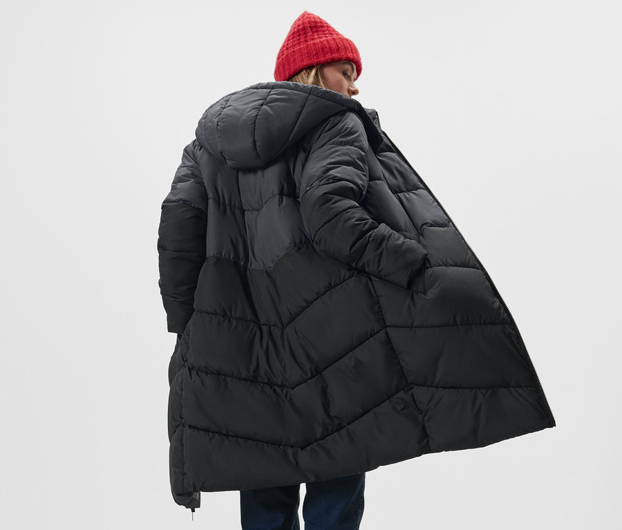 Frau trägt einen Steppmantel mit Kapuze und eine rote Mütze.