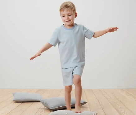 Ein Junge balanciert in einem Kinder-Shorty-Pyjama auf einem Kissen.
