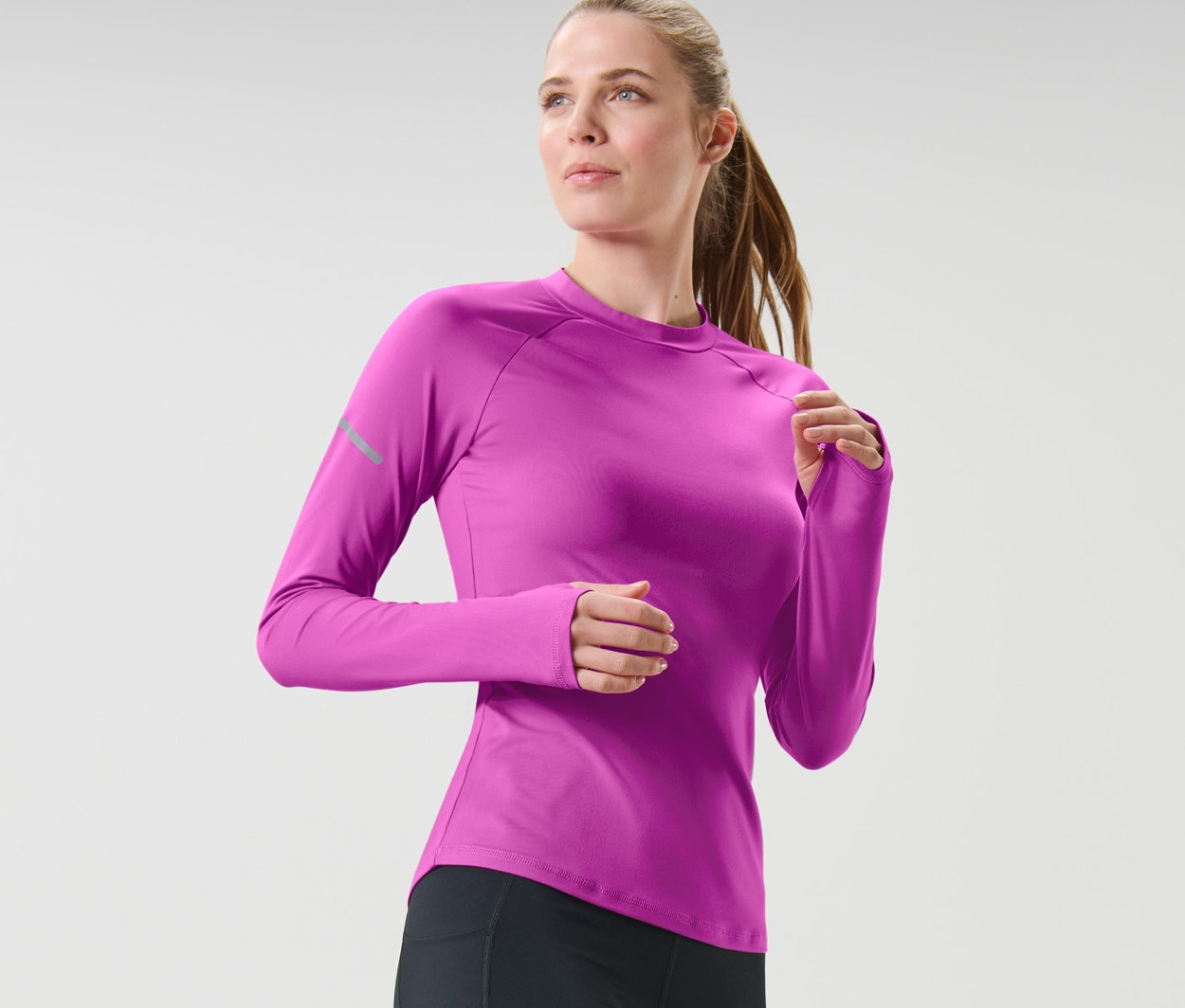 Frau in schwarzen Leggings und neonbeerfarbenem Langarm-Funktionsshirt beim Laufen.