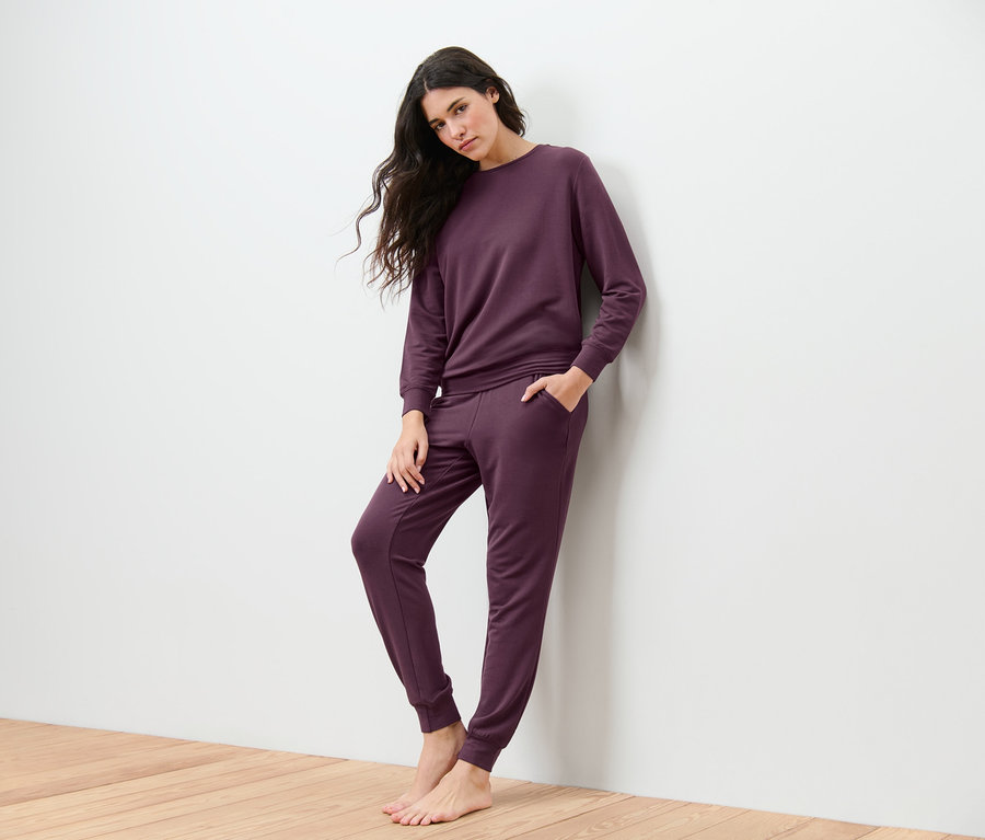 Frau lehnt an der Wand und trägt einen Hausanzug.