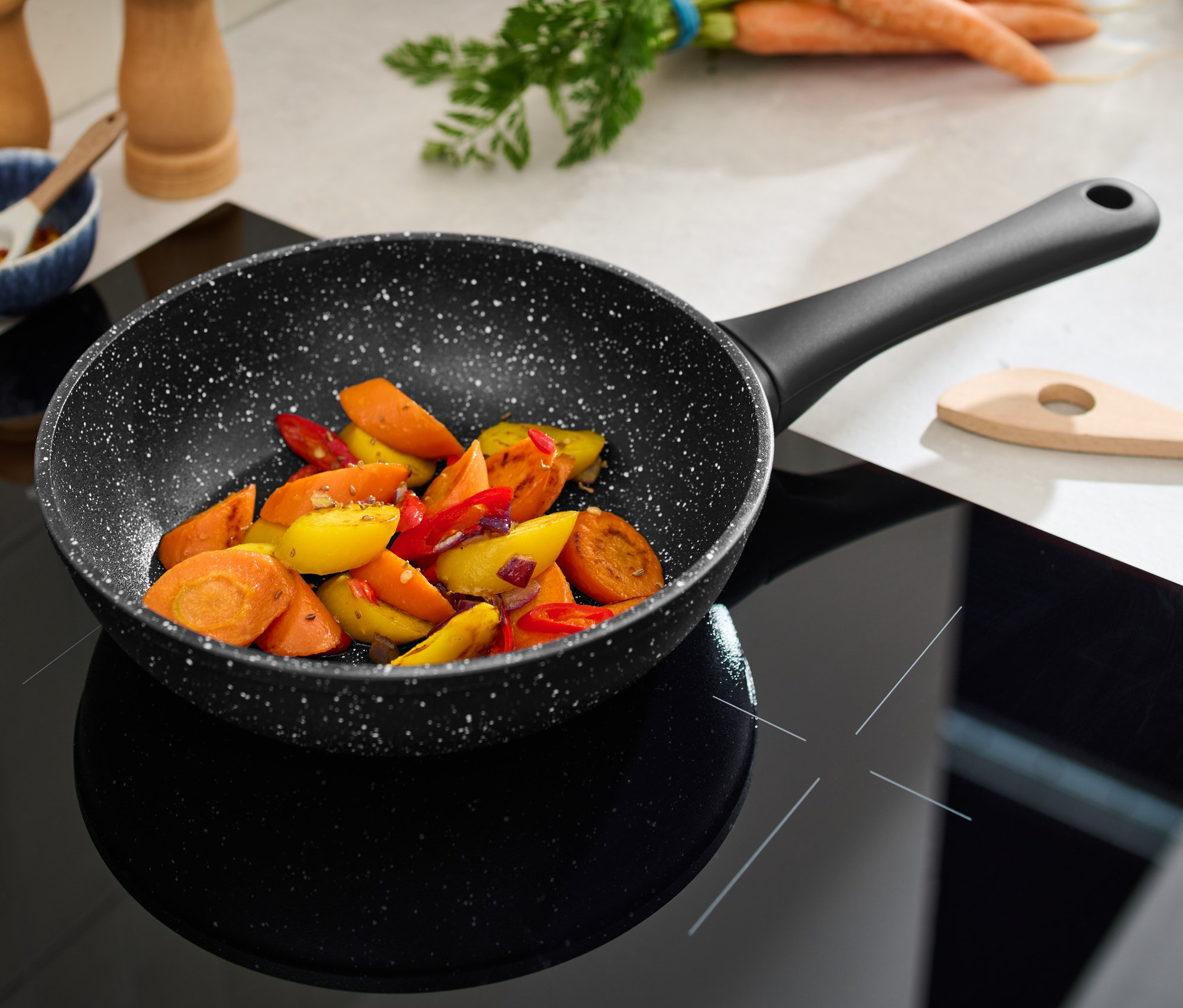 Profi-Pfanne in Steinoptik, 20 cm Durchmesser, steht auf einem schwarzen Glaskeramikkochfeld mit geschnittenem Gemüse.