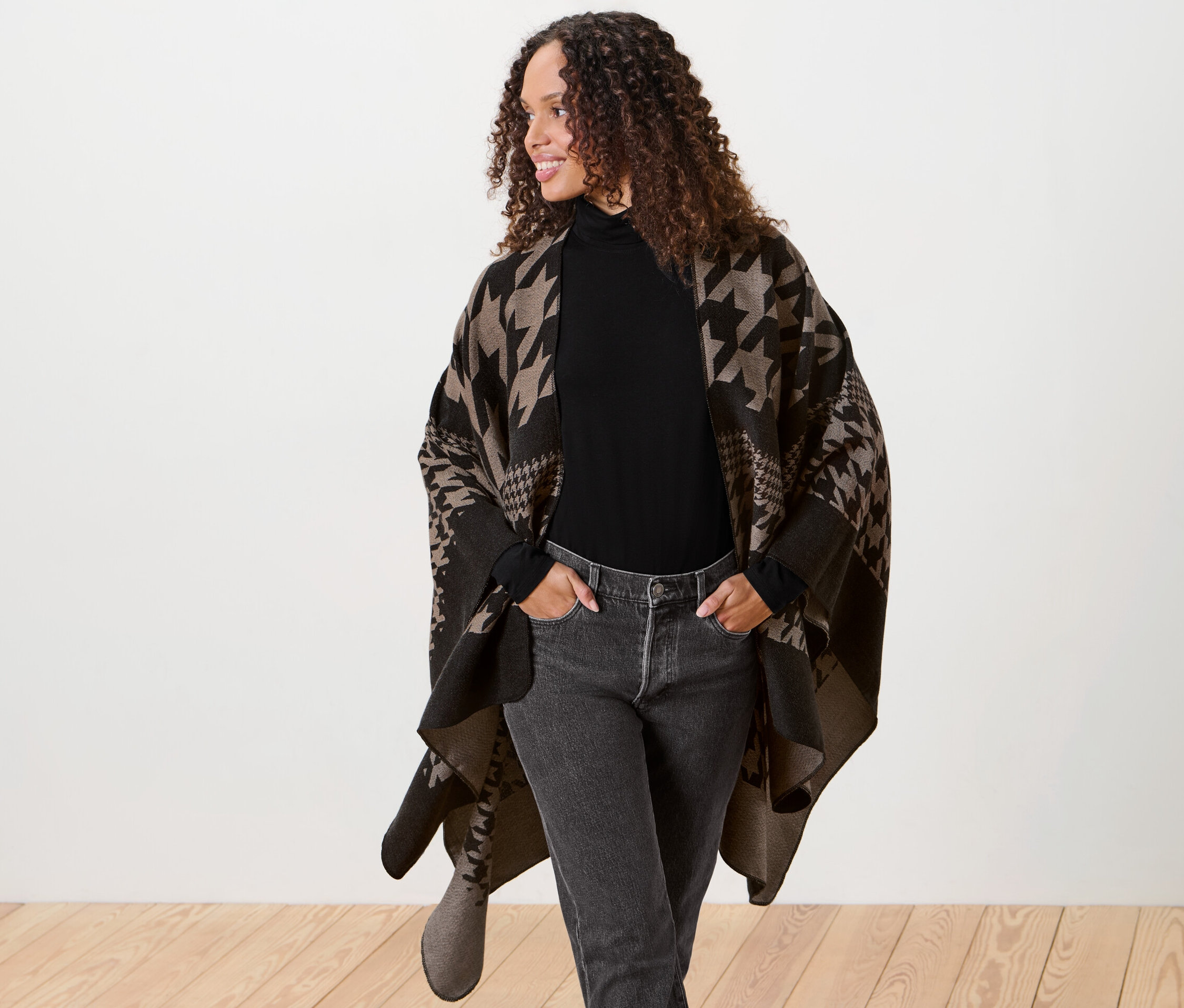 Frau mit braunen lockigen Haaren posiert in einem Poncho.