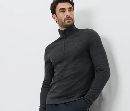 Mann posiert vor weissem Hintergrund und trägt ein Funktionsshirt mit RWS-zertifizierter Wolle und dunkle Hosen.
