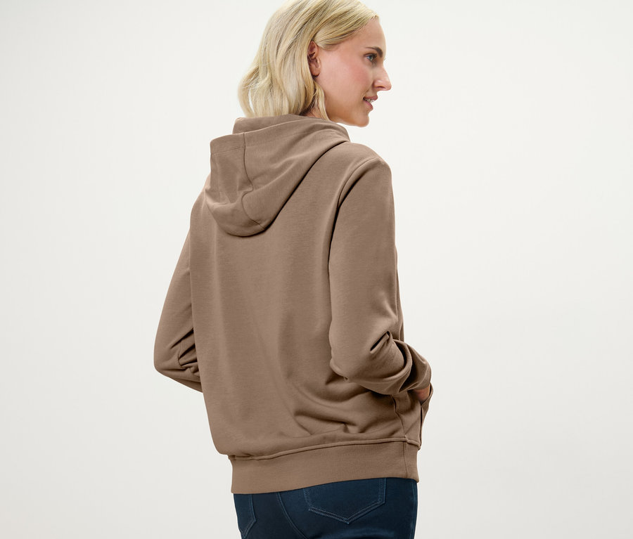 Blonde Frau trägt einen beige Hoodie.