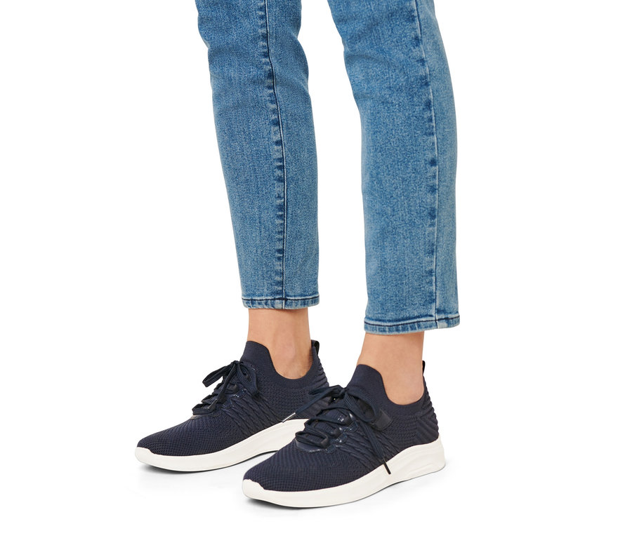 Beine einer Person in Jeans und blauen Slip-on-Sneakern mit weißen Sohlen.