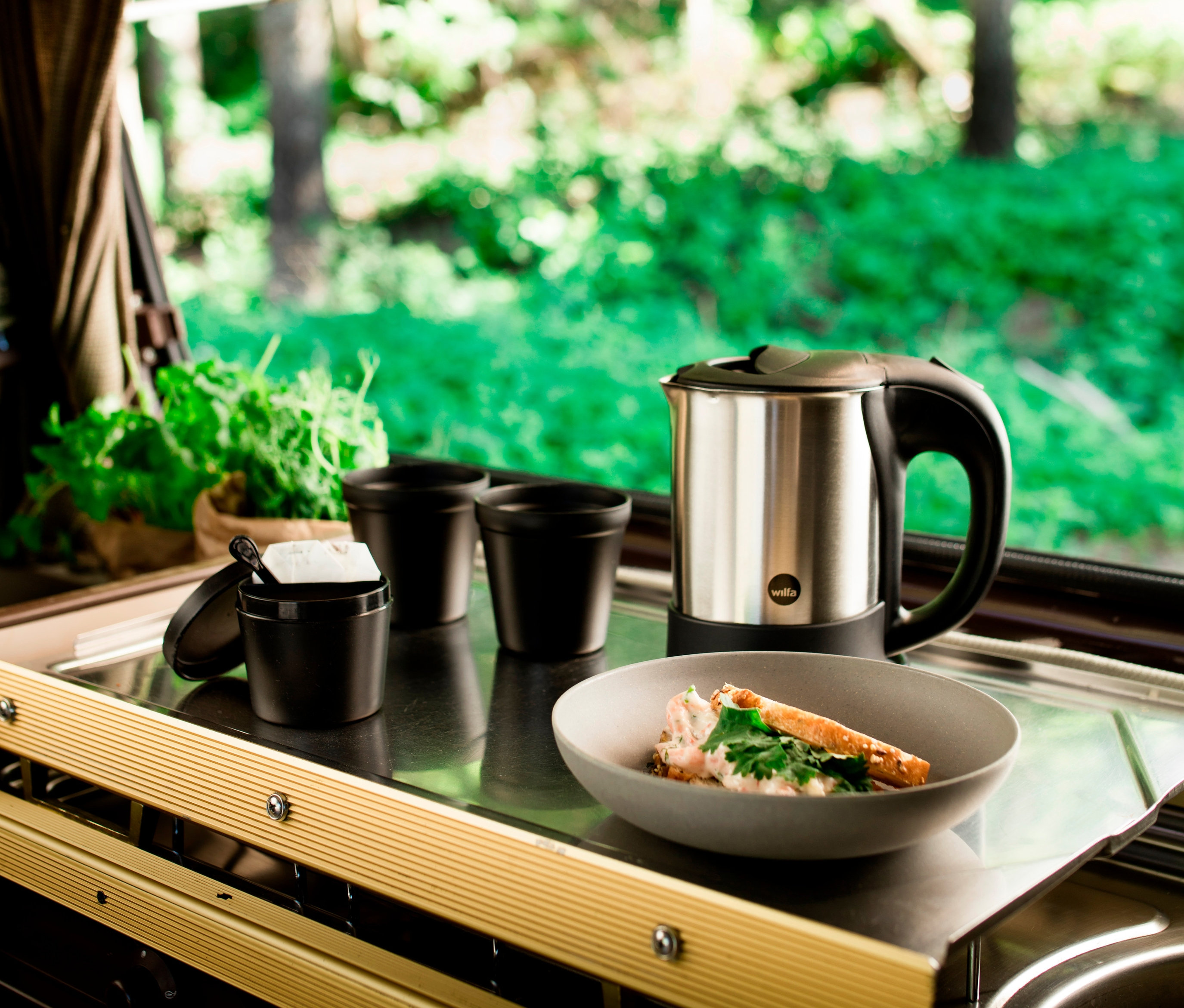 Ein Wilfa Wasserkocher TRAVEL, »TK-1000« aus Edelstahl steht auf einer Theke neben zwei schwarzen Tassen und einer Schüssel mit Essen.