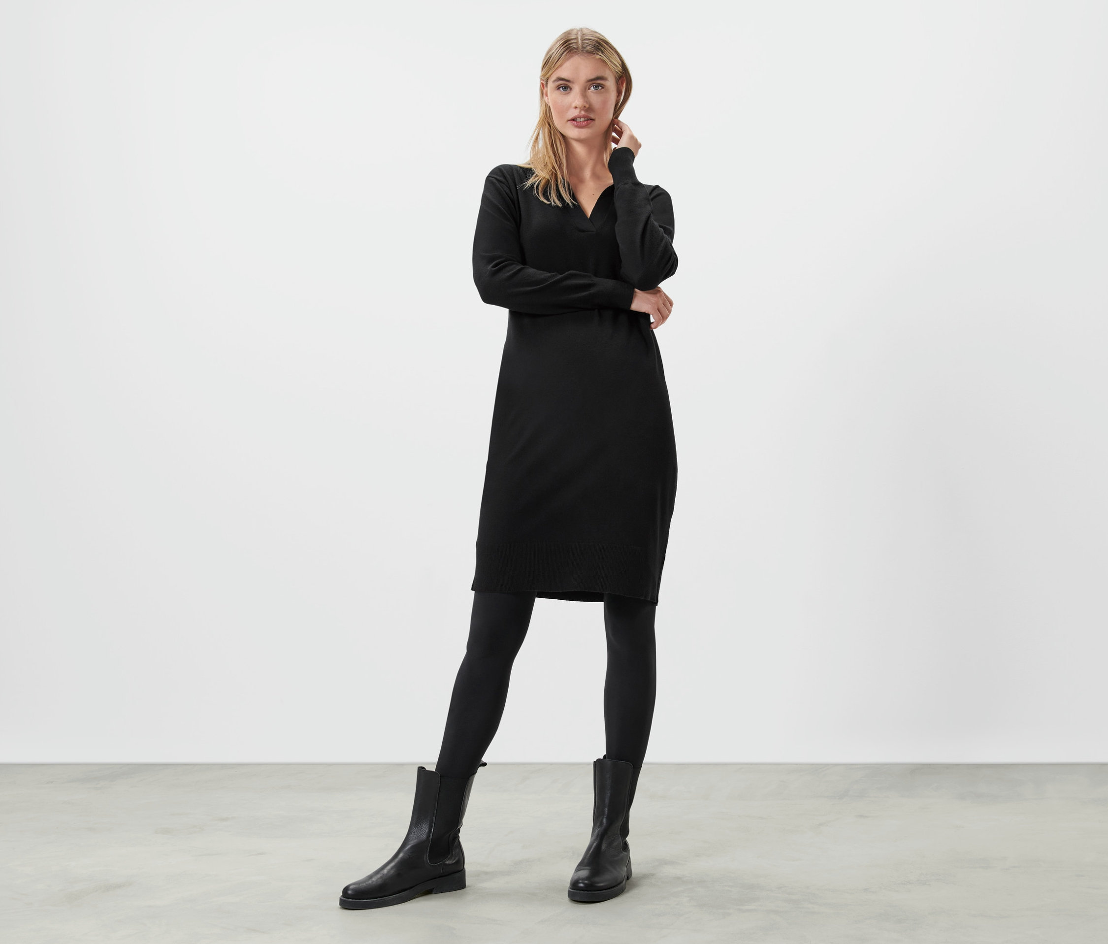 Blonde Frau steht und posiert in einem schwarzen Strickkleid.