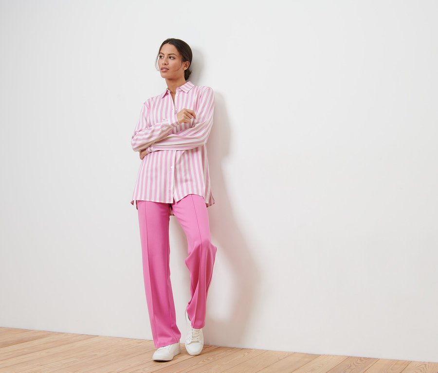 Frau posiert in rosa Hose und gestreifter Bluse.