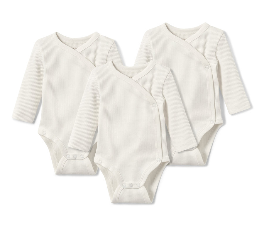 Drei weiße Baby-Ripp-Langarmbodys liegen auf einem weißen Untergrund.