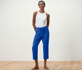 Frau posiert in weißem Top und blauer Pyjamahose.