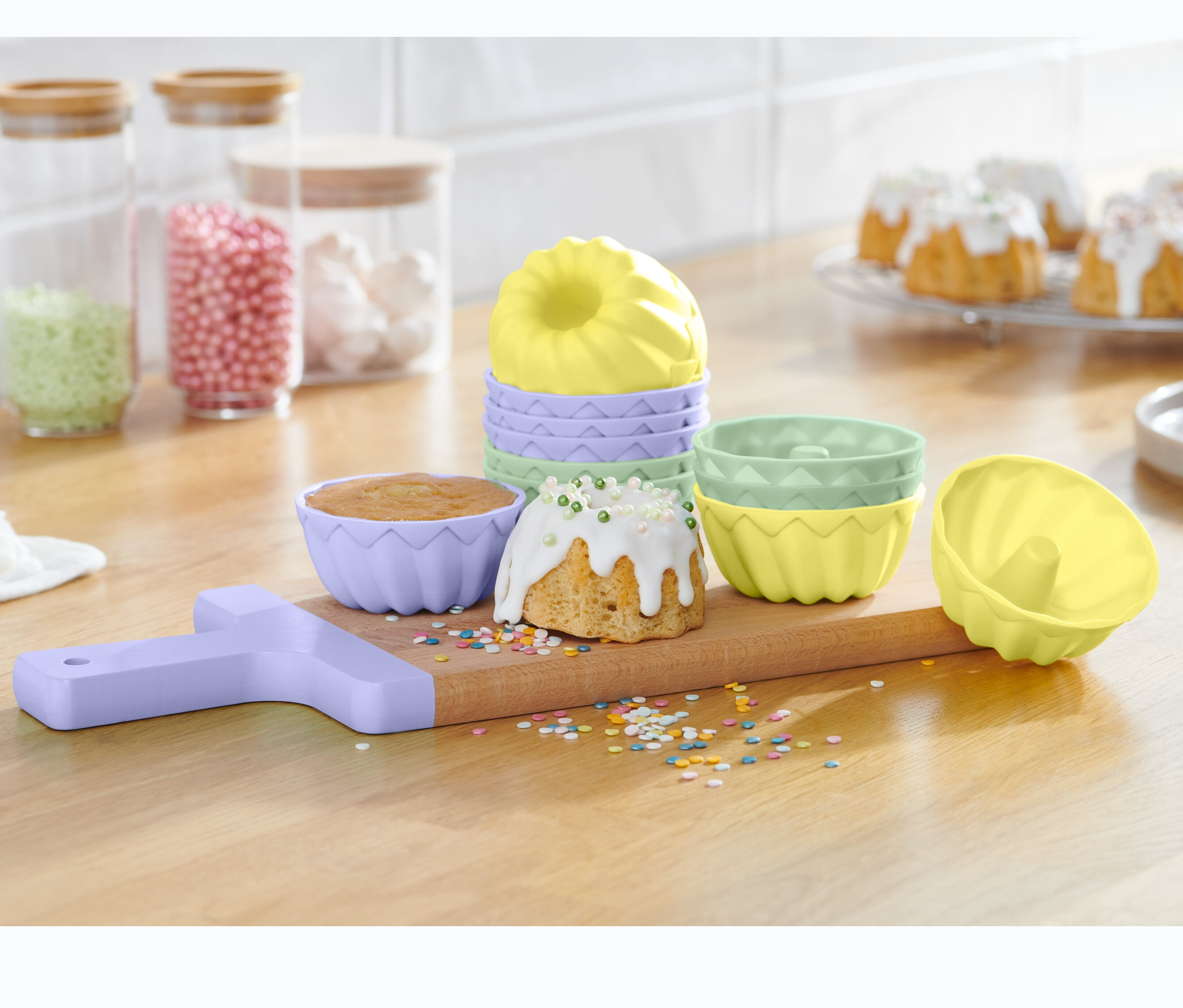 Auf einem Holzbrett stehen 12 Mini-Gugelhupfformen zusammen mit gebackenen Gugelhupfen und Streuseln.